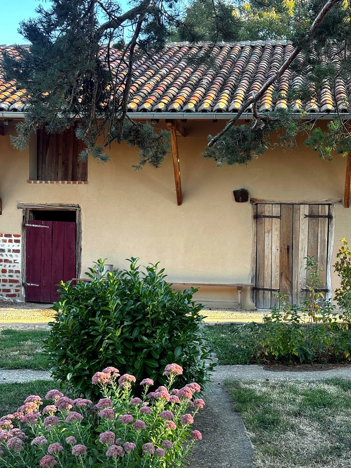 La grange au toit de tuiles, entourée de fleurs et de verdure